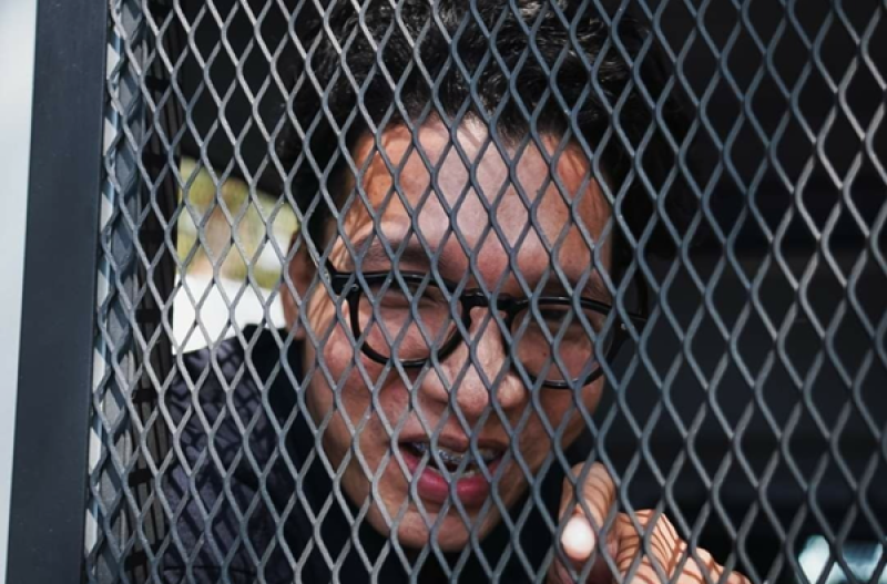 Freelance news photographer Nattaphon “Ya” Phanphongsanon talks to reporters from a police detention vehicle shortly after his arrest in Bangkok on 12 February 2024. Image by Ginger Cat, Prachatai