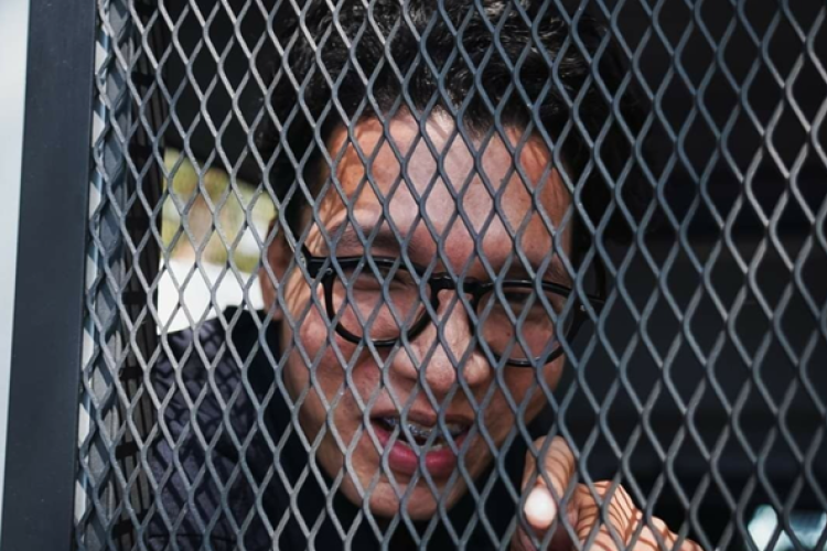 Freelance news photographer Nattaphon “Ya” Phanphongsanon talks to reporters from a police detention vehicle shortly after his arrest in Bangkok on 12 February 2024. Image by Ginger Cat, Prachatai